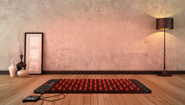 PEMF grounding mat with controller on a wooden floor glowing from red light therapy LEDs.