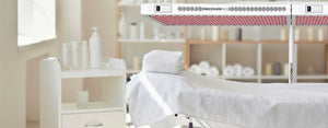 Wellness center room with red light therapy device called the Beam over a towel covered bed.