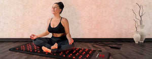 Young woman enjoying a PEMF mat while meditating. Sitting indian style touching fingers.