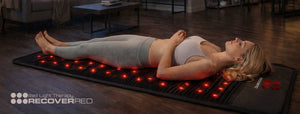 Woman lying on a red light therapy mat in a room with wooden flooring.