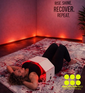 Person lying on a rug with a red light therapy device, surrounded the mid section.