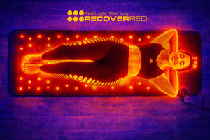 Red light therapy PEMF mat with a woman lying on it, glowing with red light, against a dark purple floor.
