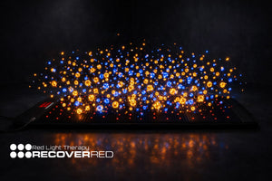 Red light therapy mat with glowing blue and orange lights on a dark background, featuring the Recovered brand.