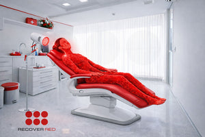 Person lying on a red recliner chair in a modern room with a targeted red light therapy device on a stand.